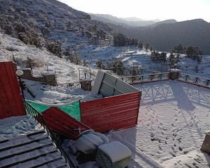 A snow-covered outdoor area with a red wooden structure, possibly a deck or patio, surrounded by snow-covered steps and a railing.