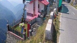 A house with a red roof and pink walls, located on a hillside with a road nearby. - Veenu's Cottage (Dehradun)