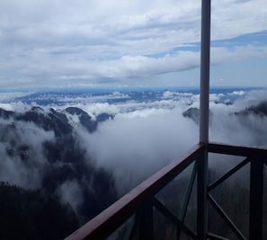 A panoramic view from a high vantage point, likely a mountain observation deck, overlooking a valley with dense forests and a layer of clouds below.