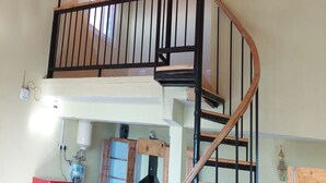 A spacious room with a wooden ceiling, a spiral staircase with black railings, and a view of the outdoors through a window. - Veenu's Cottage (Dehradun)