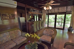 A cozy living area with wicker furniture, a ceiling fan, and a view of greenery outside.