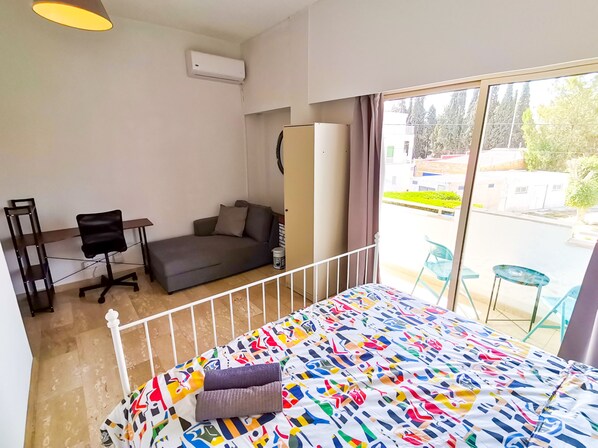 A bedroom with a bed, a sofa, a desk, and a chair. There is a window with a view of the outside. - Central Square Nomadic Rooms (Larnaca)