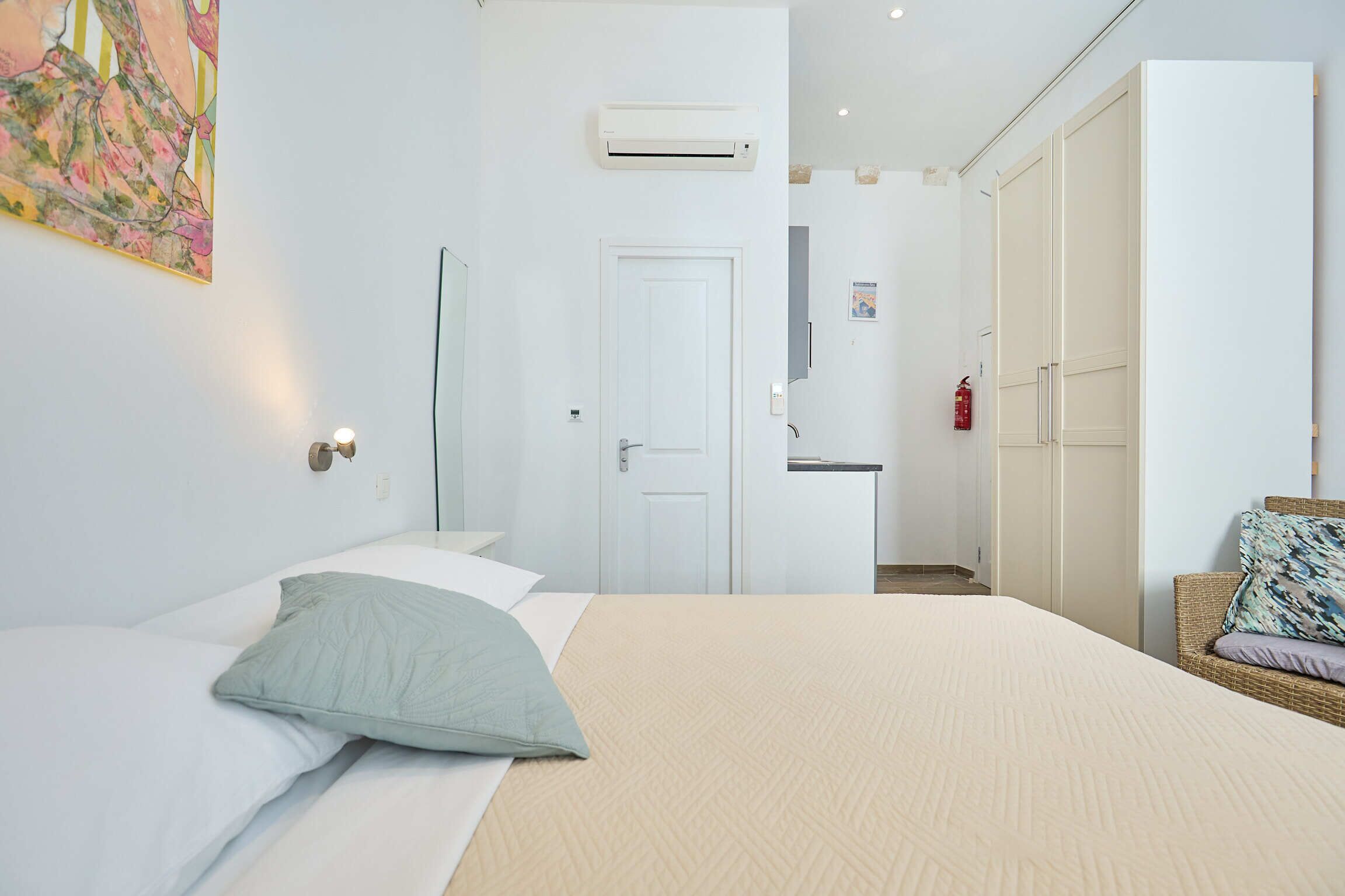 A bedroom with a bed, a wardrobe, an air conditioning unit, and a small kitchenette.
