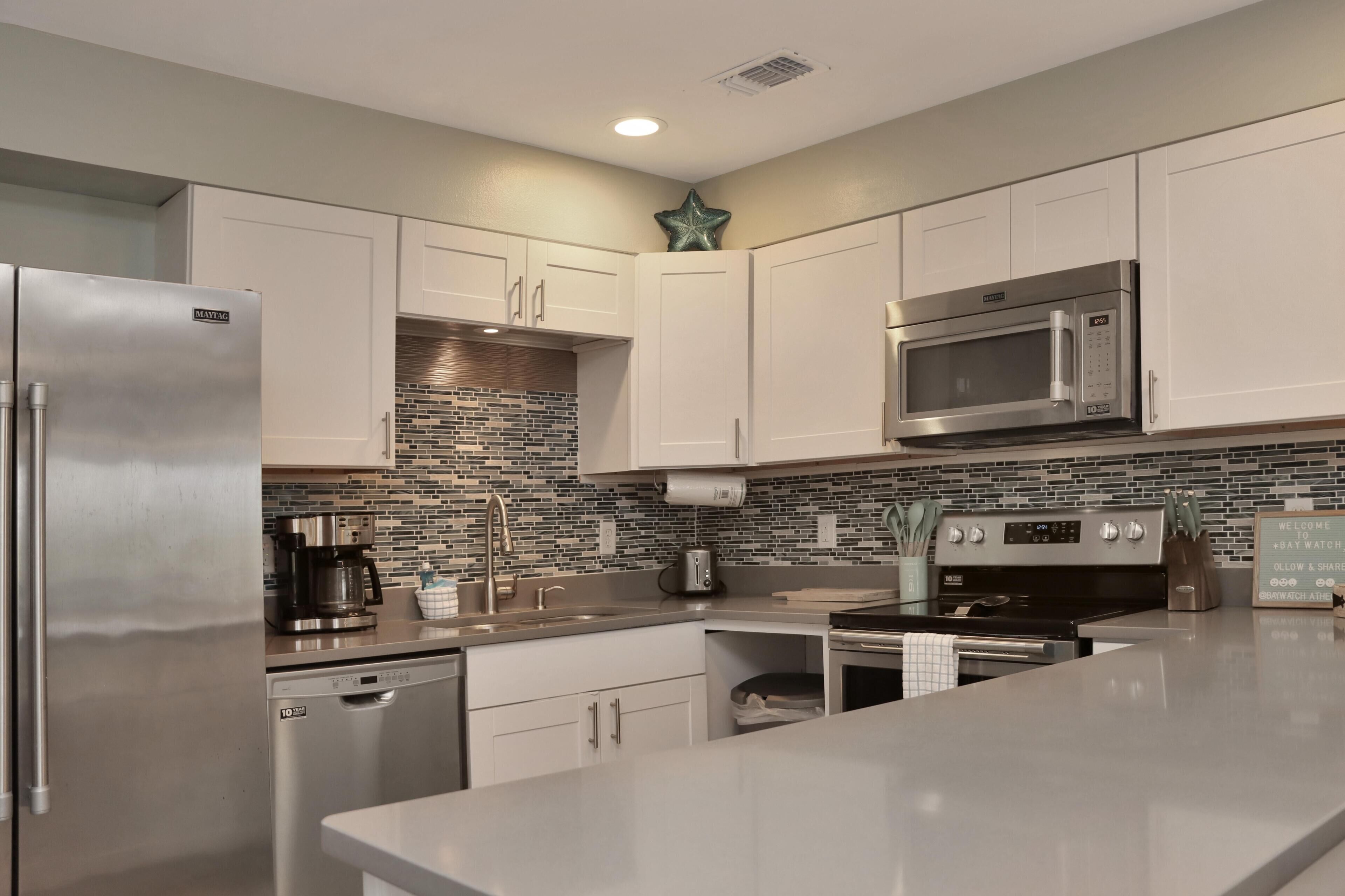 A modern kitchen with stainless steel appliances, white cabinetry, a brick backsplash, and a large island.
