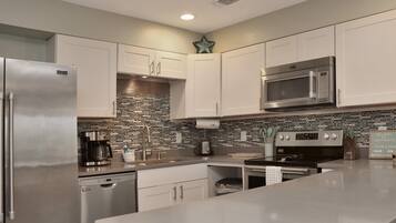 A modern kitchen with stainless steel appliances, white cabinetry, a brick backsplash, and a large island.