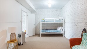 A room with a bunk bed, a chair, a radiator, and a door.