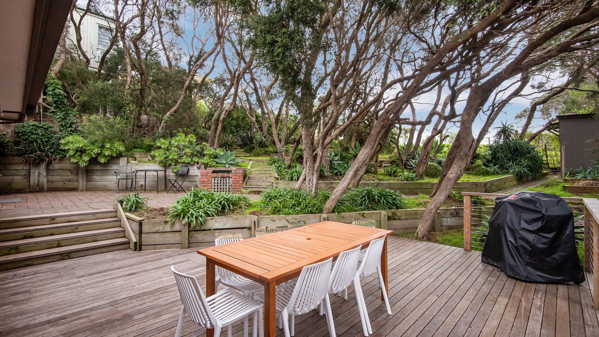 A wooden deck with a table and chairs, surrounded by lush greenery and trees.