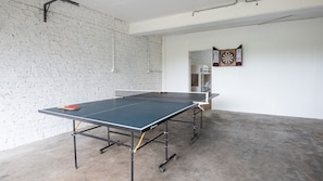 A ping pong table with a dartboard and a clock on the wall in a room with a white brick wall.