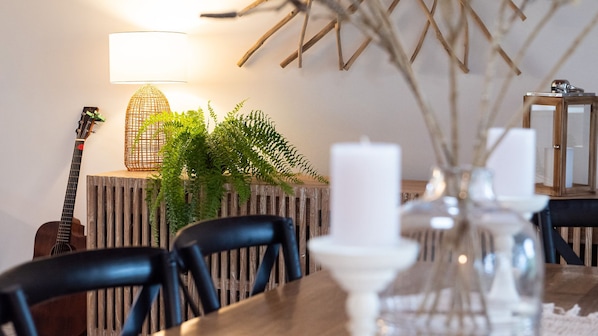 A dining area with a wooden table, chairs, a guitar, a lamp, and a plant.
