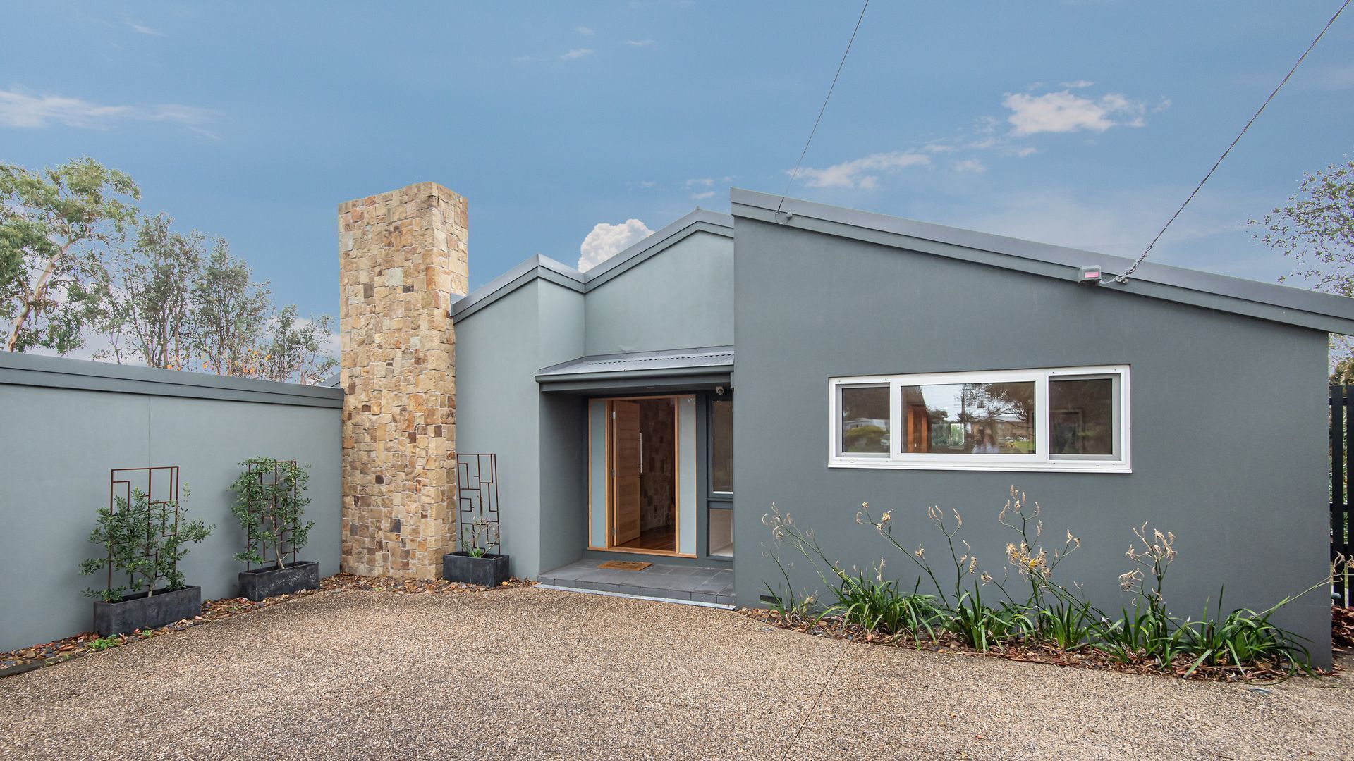 Una casa moderna con chimenea de piedra, fachada gris y entrada con camino de grava.