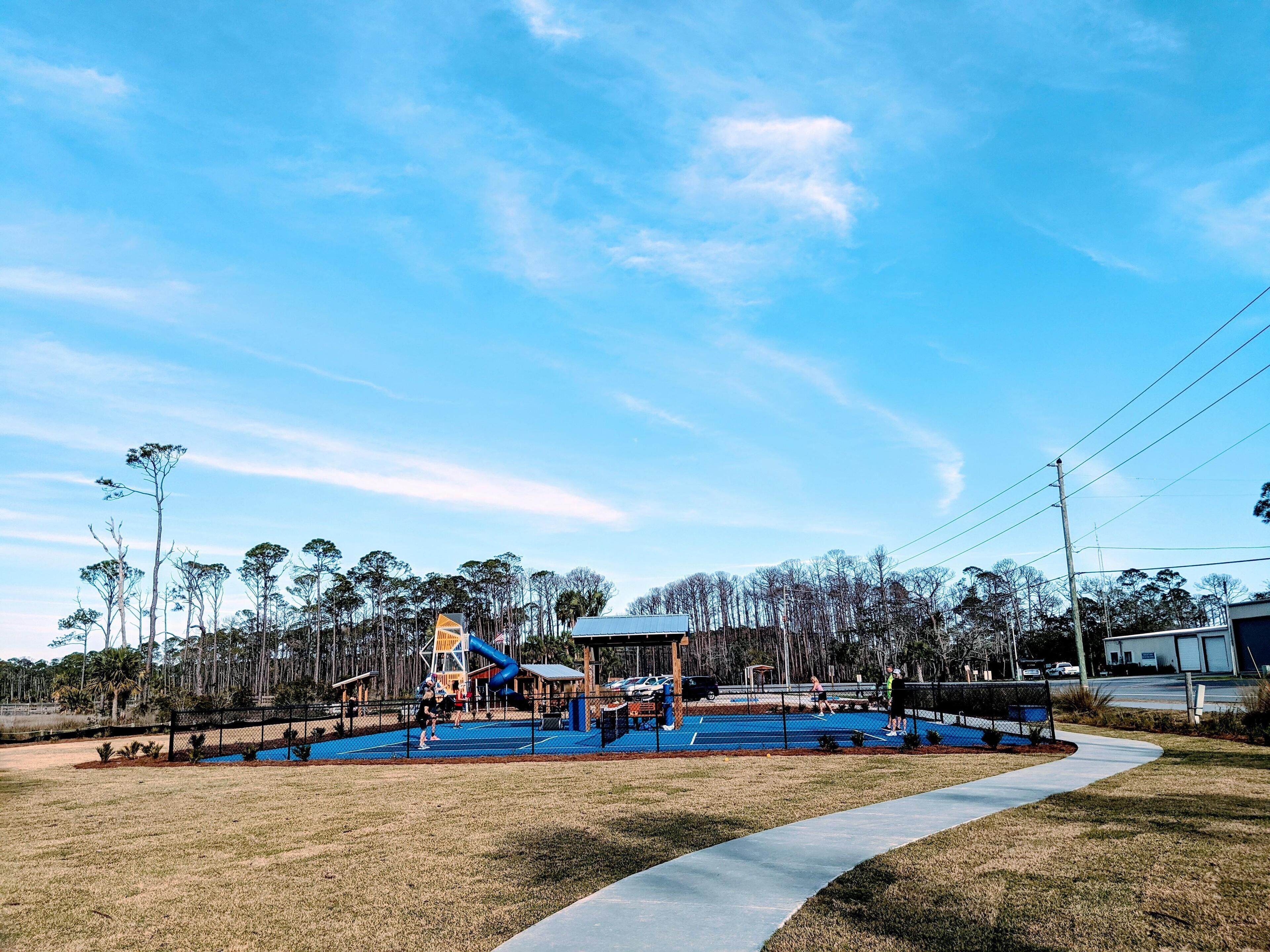 A playground with a blue climbing structure, surrounded by trees and a clear sky.