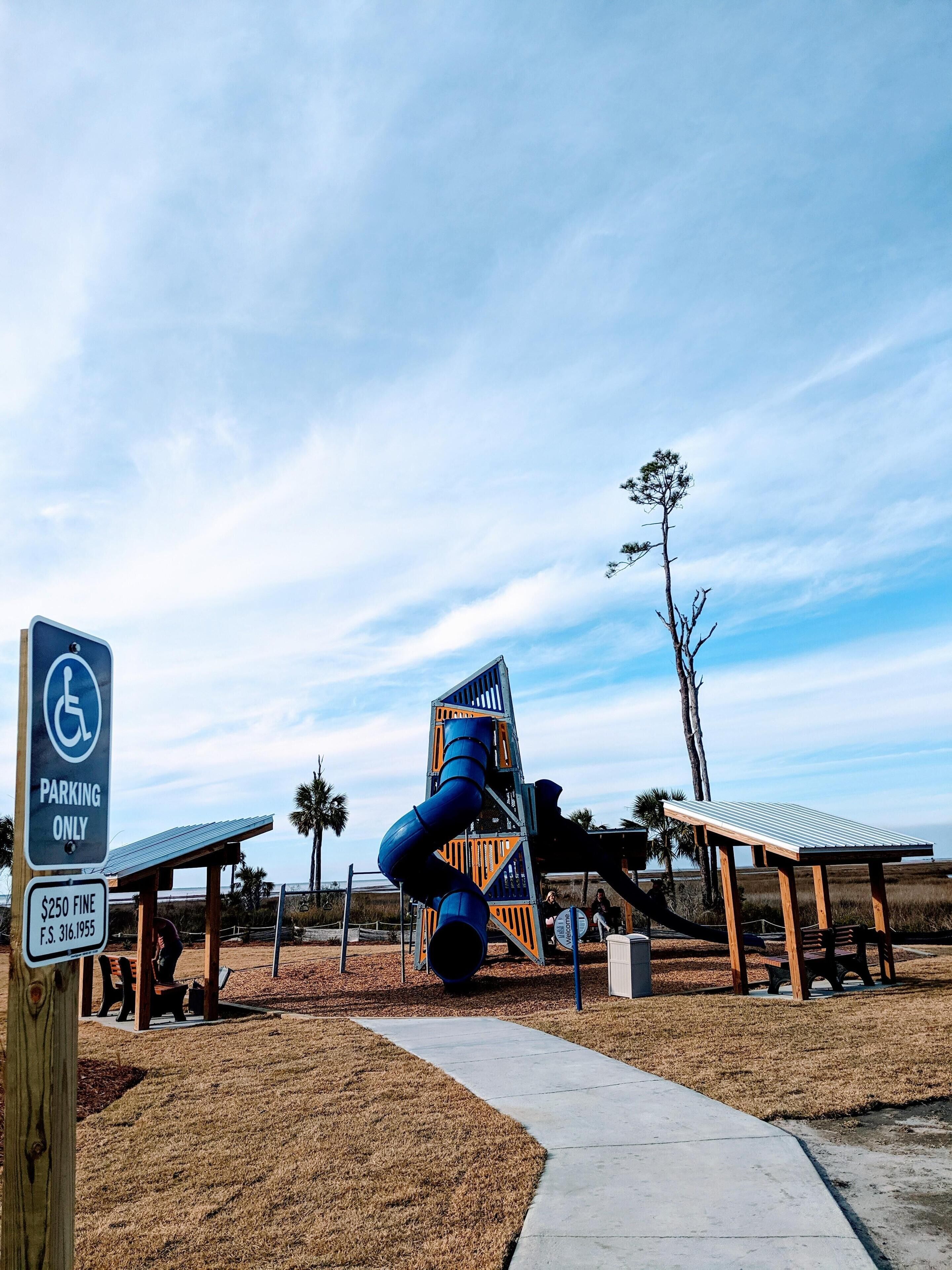 A playground with a blue spiral slide, a wheelchair-accessible sign, and a covered seating area.