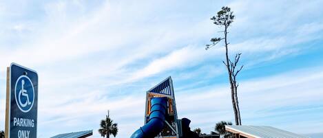 A playground with a blue spiral slide, a wheelchair-accessible sign, and a covered seating area.
