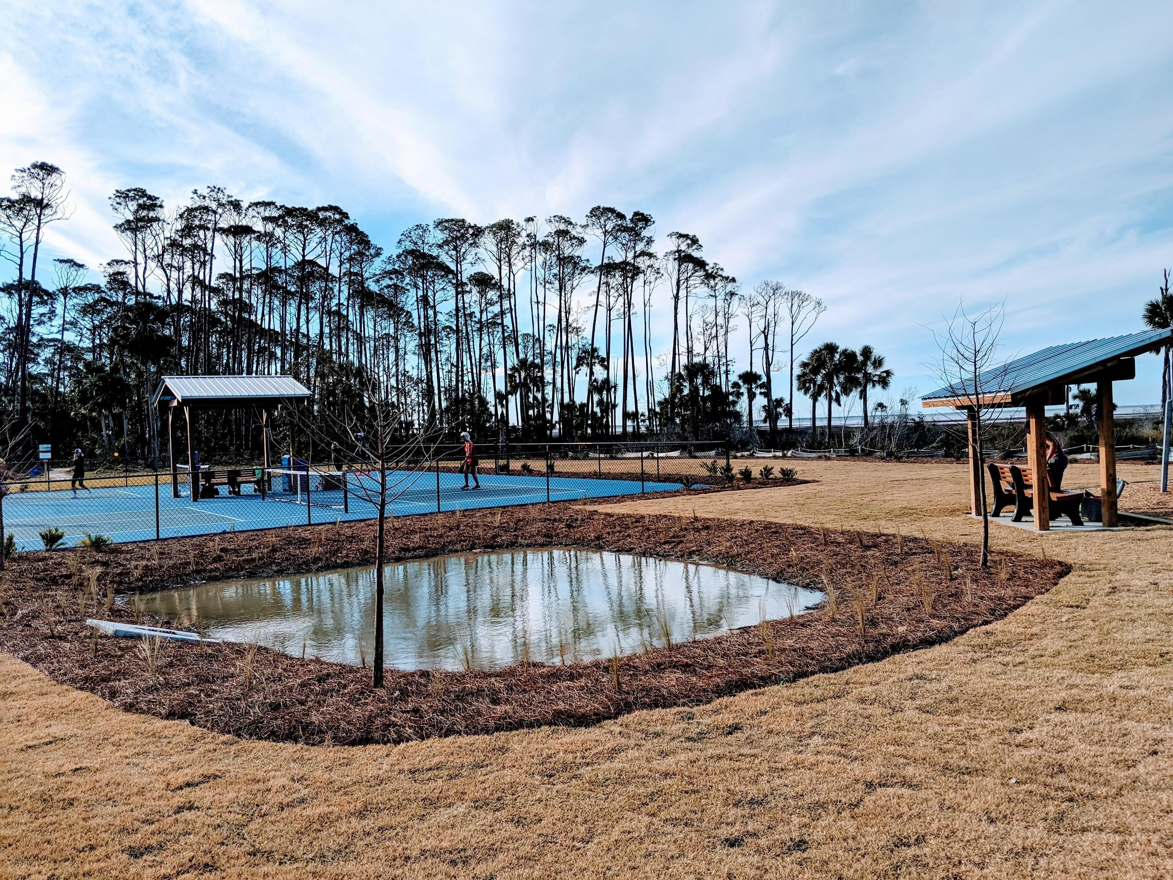 A park with a tennis court, a small pond, and a pavilion.
