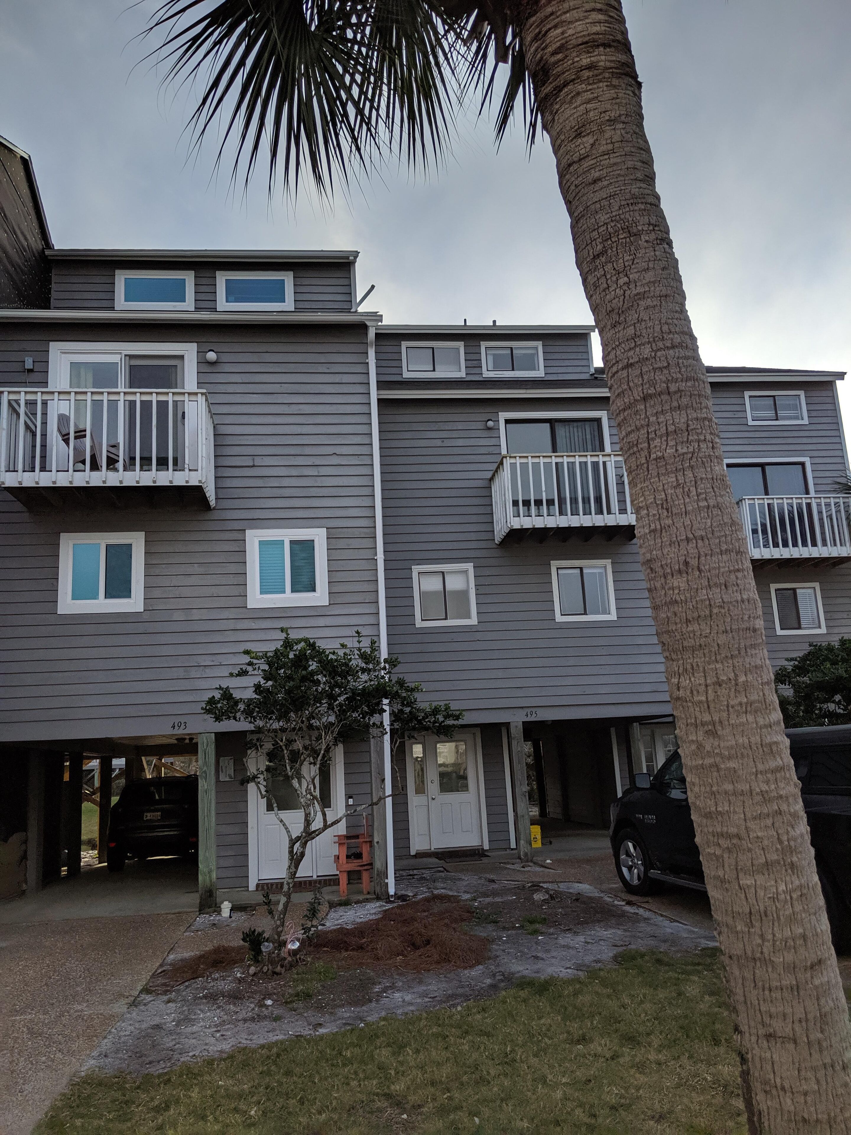 A multi-story residential building with balconies, a small front yard, and a palm tree.
