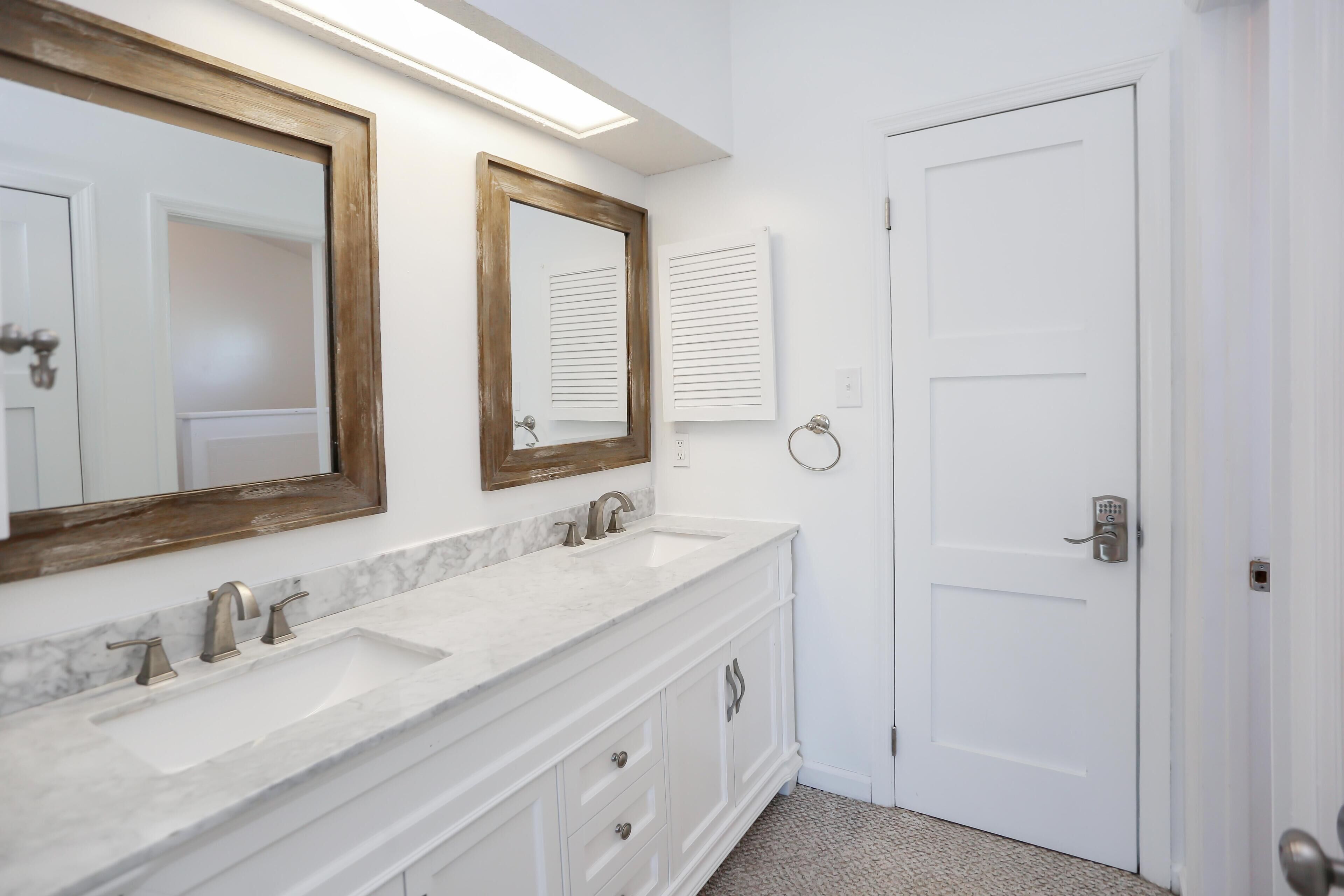 A bathroom with two sinks, a large mirror, and a door with a lock.