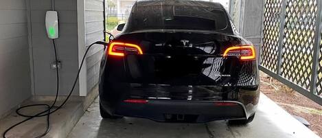 A black car parked in a covered parking area with a charging station on the wall.