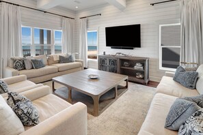 A spacious living room with a large flat-screen TV, a beige sofa set, a coffee table, and a wooden cabinet with decorative items.