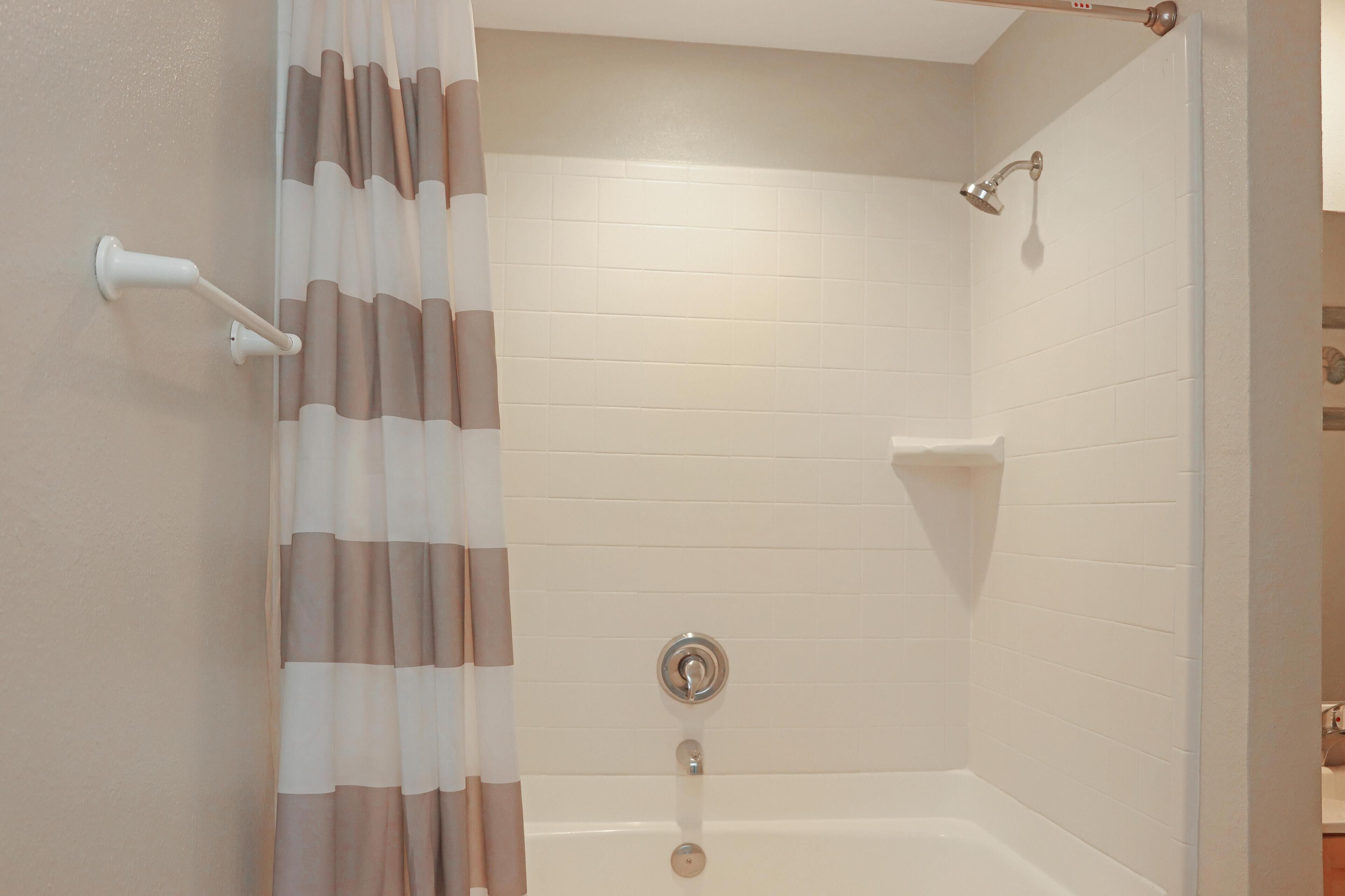 A shower with a curtain, a handheld showerhead, and a wall-mounted control.