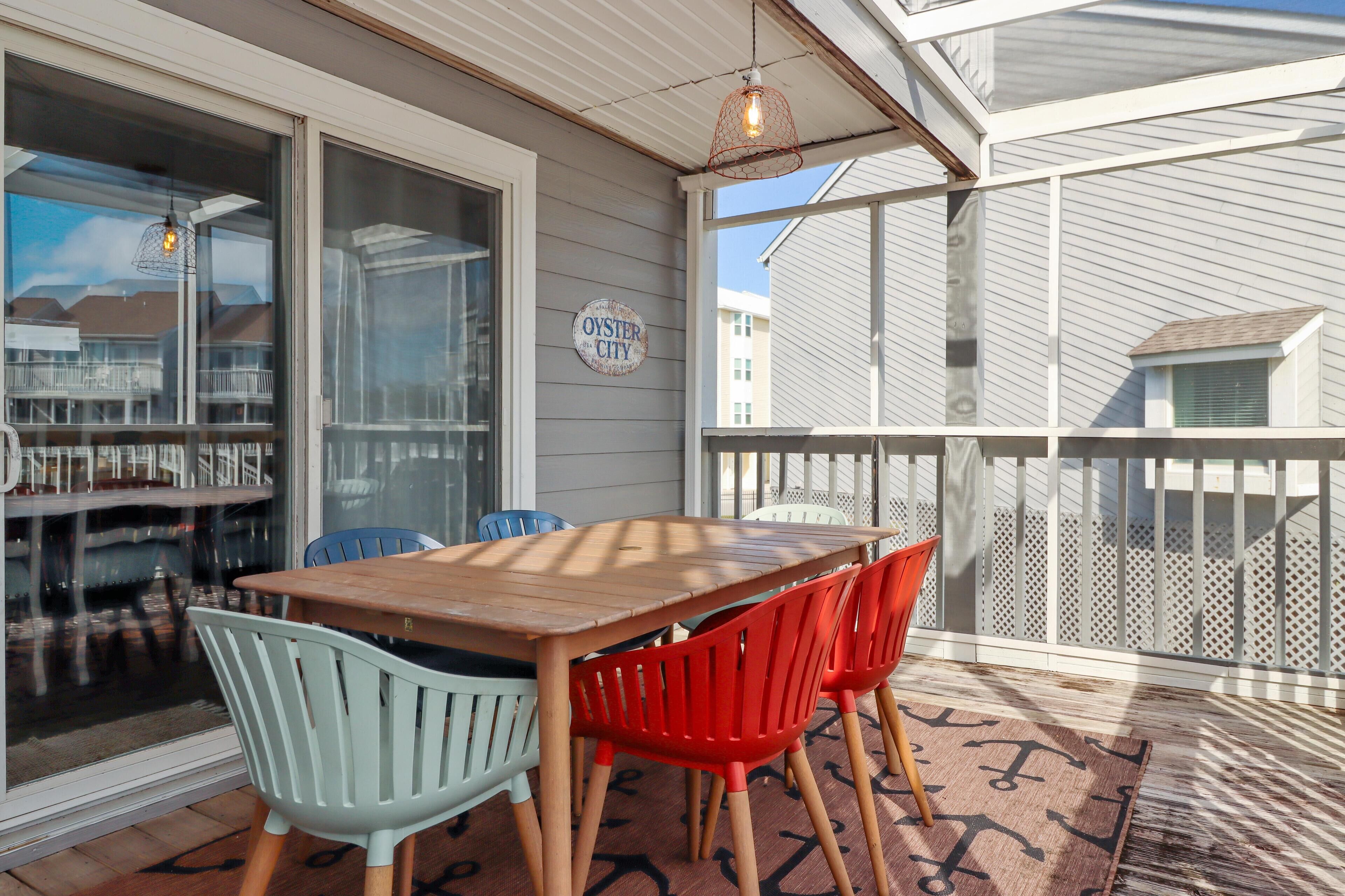 Een overdekt terras met een houten tafel en stoelen, een bord met de tekst 'Oyster City' en een uitzicht op omliggende huizen.