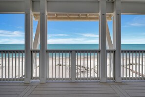 Une terrasse en bois couverte, offrant une vue sur une plage et l’océan.
