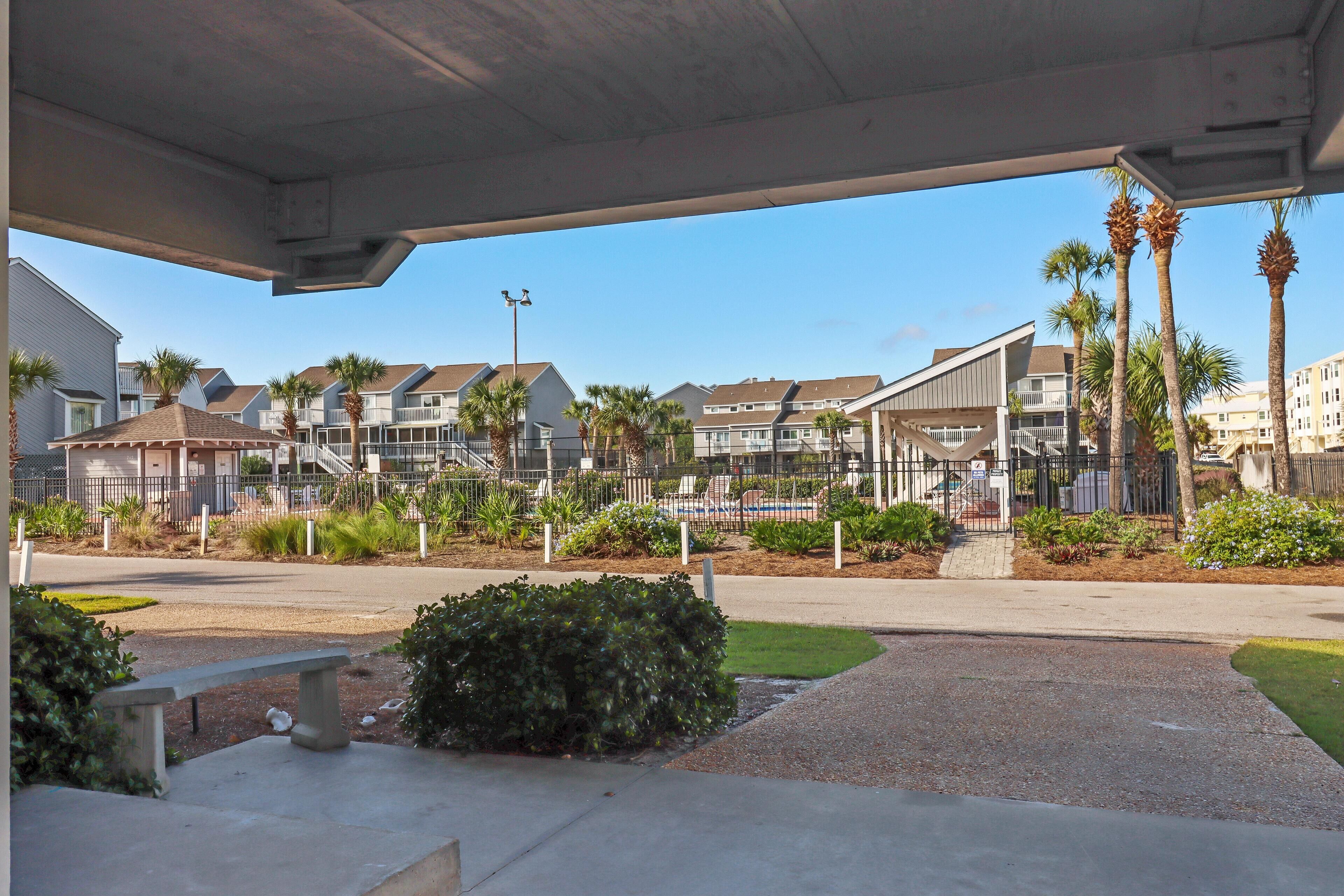 A covered outdoor area with a concrete bench, palm trees, and a view of residential buildings in the background.
