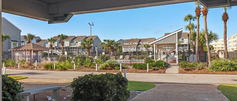 A covered outdoor area with a concrete bench, palm trees, and a view of residential buildings in the background.