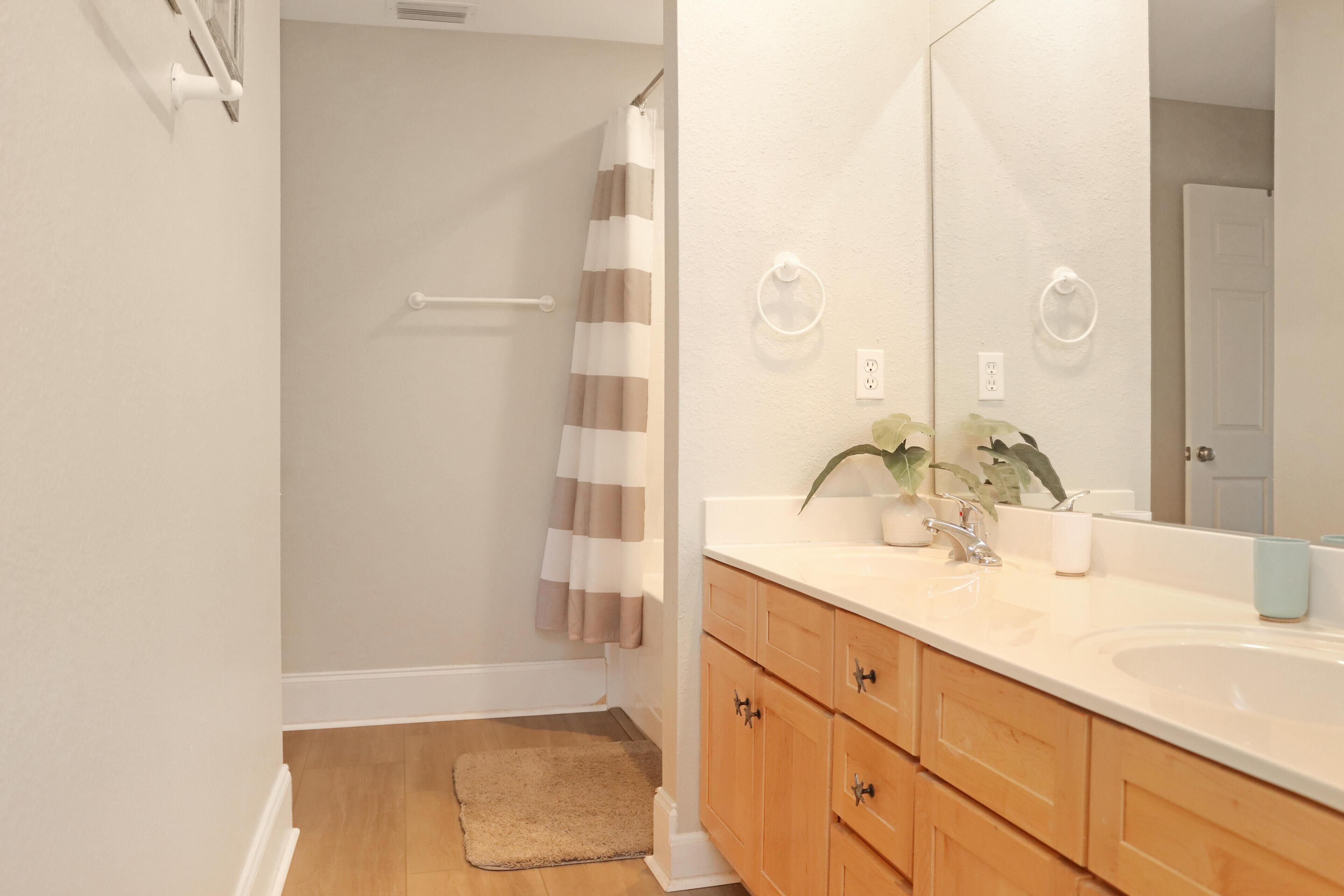 A bathroom with a wooden vanity, a large mirror, and a shower with a striped curtain.