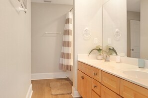 A bathroom with a wooden vanity, a large mirror, and a shower with a striped curtain. - Barrier Dunes 248 - 111 Endless Summer (Port St. Joe)