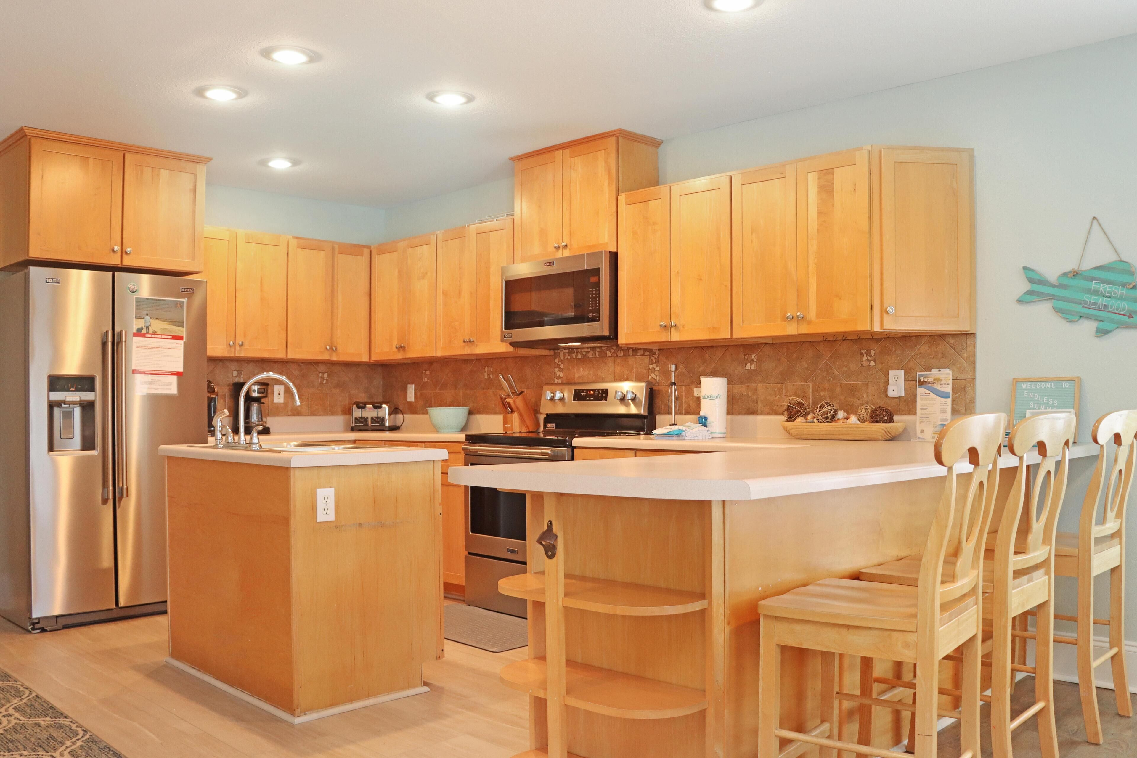 Una cocina moderna con armarios de madera, electrodomésticos de acero inoxidable y una isla central con taburetes de bar.