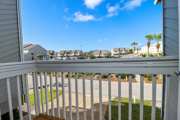A view from a balcony overlooking a residential area with multiple townhouses, a clear sky, and a well-maintained lawn.