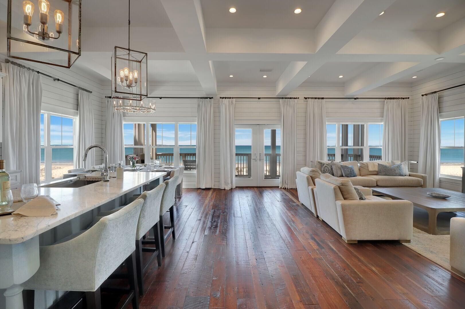 A spacious living area with a large window overlooking the beach, a dining area with a bar, and a cozy seating area with a sofa and a coffee table.