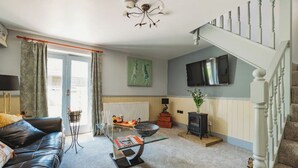Un salon avec un canapé en cuir noir, une table basse en verre, une cheminée et un escalier.