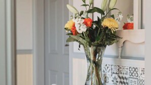 Une chaise blanche avec une pancarte « Bienvenue », un vase rempli de fleurs et un mur recouvert de carreaux décoratifs.