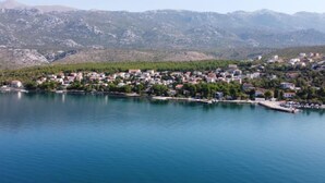 Une ville côtière avec des maisons le long du littoral, un port de plaisance et des montagnes en arrière-plan.
