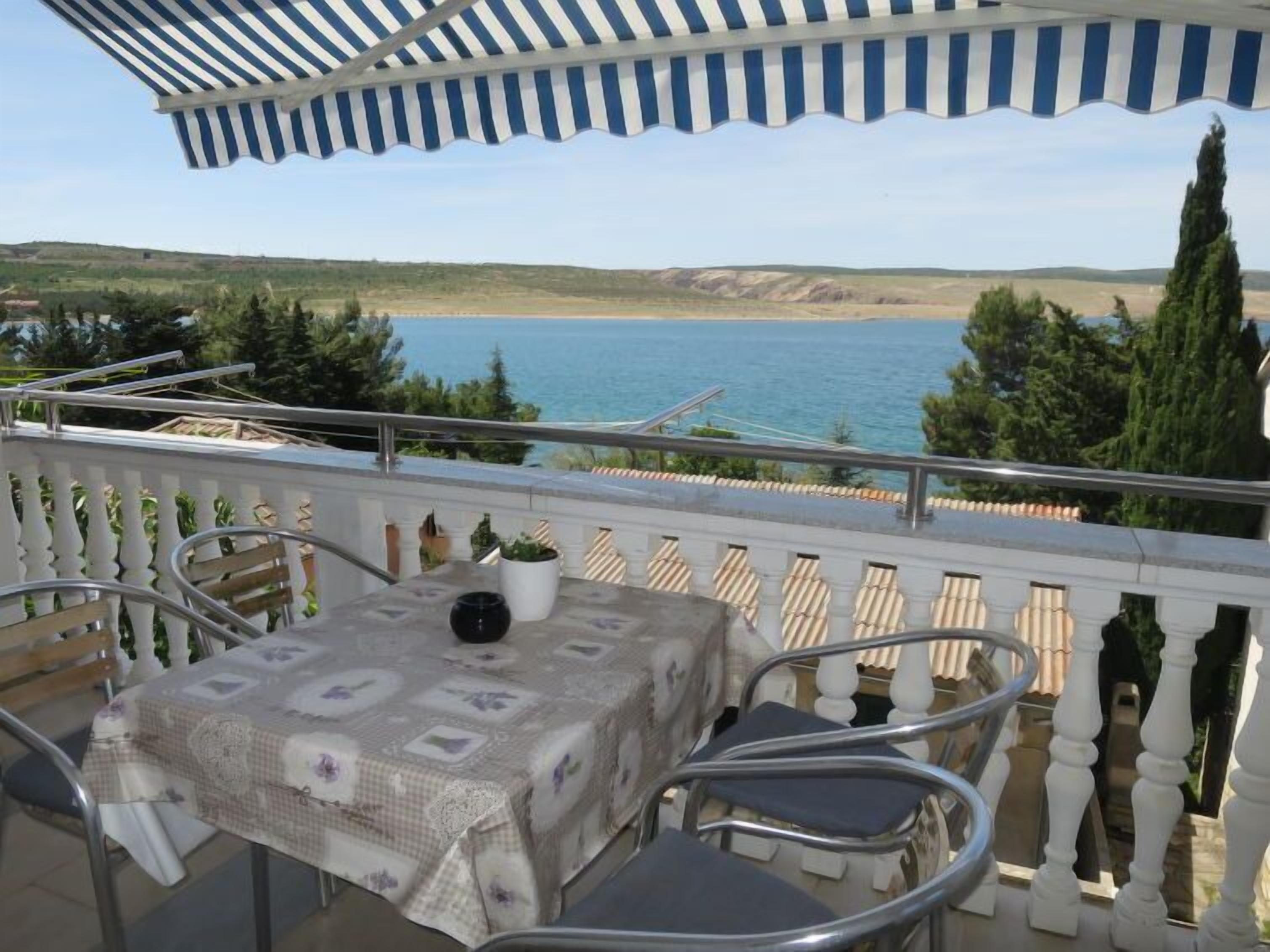 A balcony with a table and chairs, overlooking a body of water and hills.