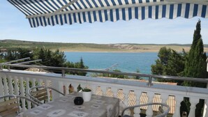 Un balcon avec une table et des chaises, donnant sur une étendue d’eau et des collines.