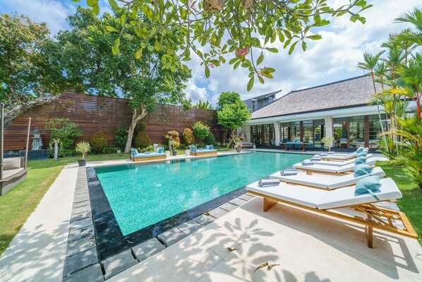 A swimming pool with lounge chairs, a wooden fence, and a house in the background.