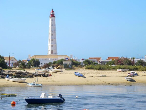 A coastal scene with a lighthouse, sandy beach, and several boats.