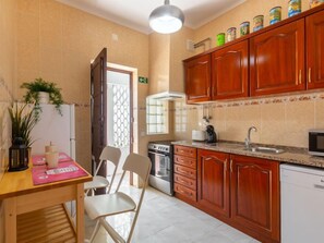 A compact kitchen with wooden cabinets, a stove, a microwave, and a sink. There is a dining table with chairs and a small plant on the counter.
