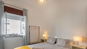 A bedroom with a bed, bedside tables, a hanging chair, and a window with curtains. - Magnolia by Interhome (Olhão)