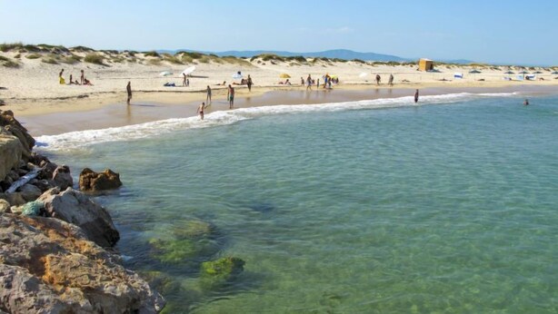 A beach with clear water, rocky shoreline, and people enjoying the beach. - Magnolia by Interhome (Olhão)