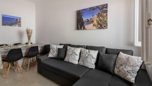 A modern living room with a black sectional sofa, a dining table with chairs, and a large landscape painting on the wall. - Magnolia by Interhome (Olhão)