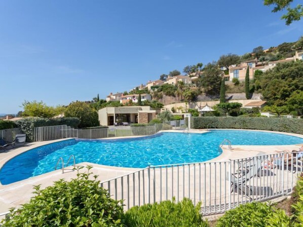 A swimming pool with a curved edge, surrounded by a metal fence, and a view of hillside houses in the background.