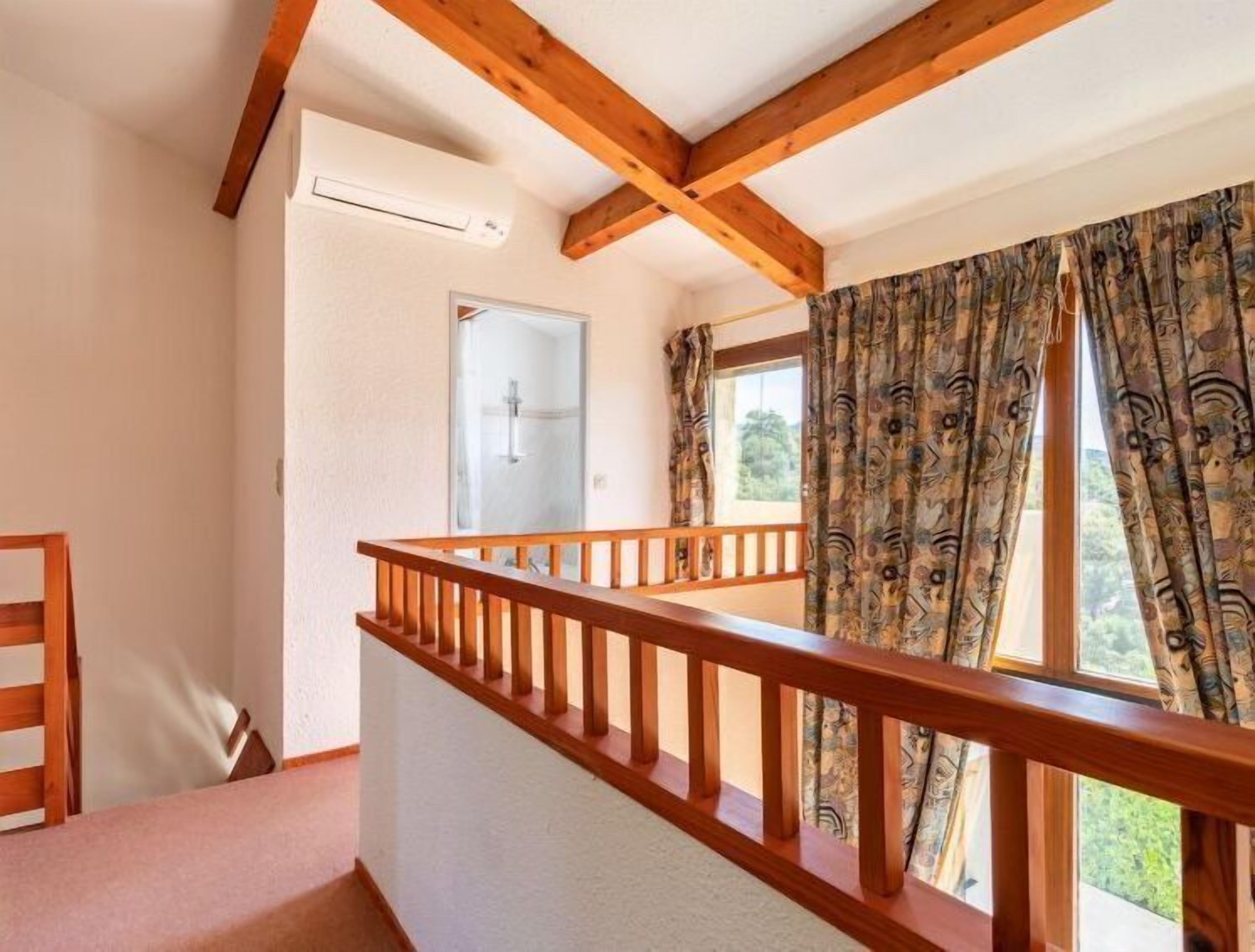 Une pièce avec une balustrade en bois sur le balcon, une porte dotée d’un panneau de verre et des rideaux à motifs sur une fenêtre.
