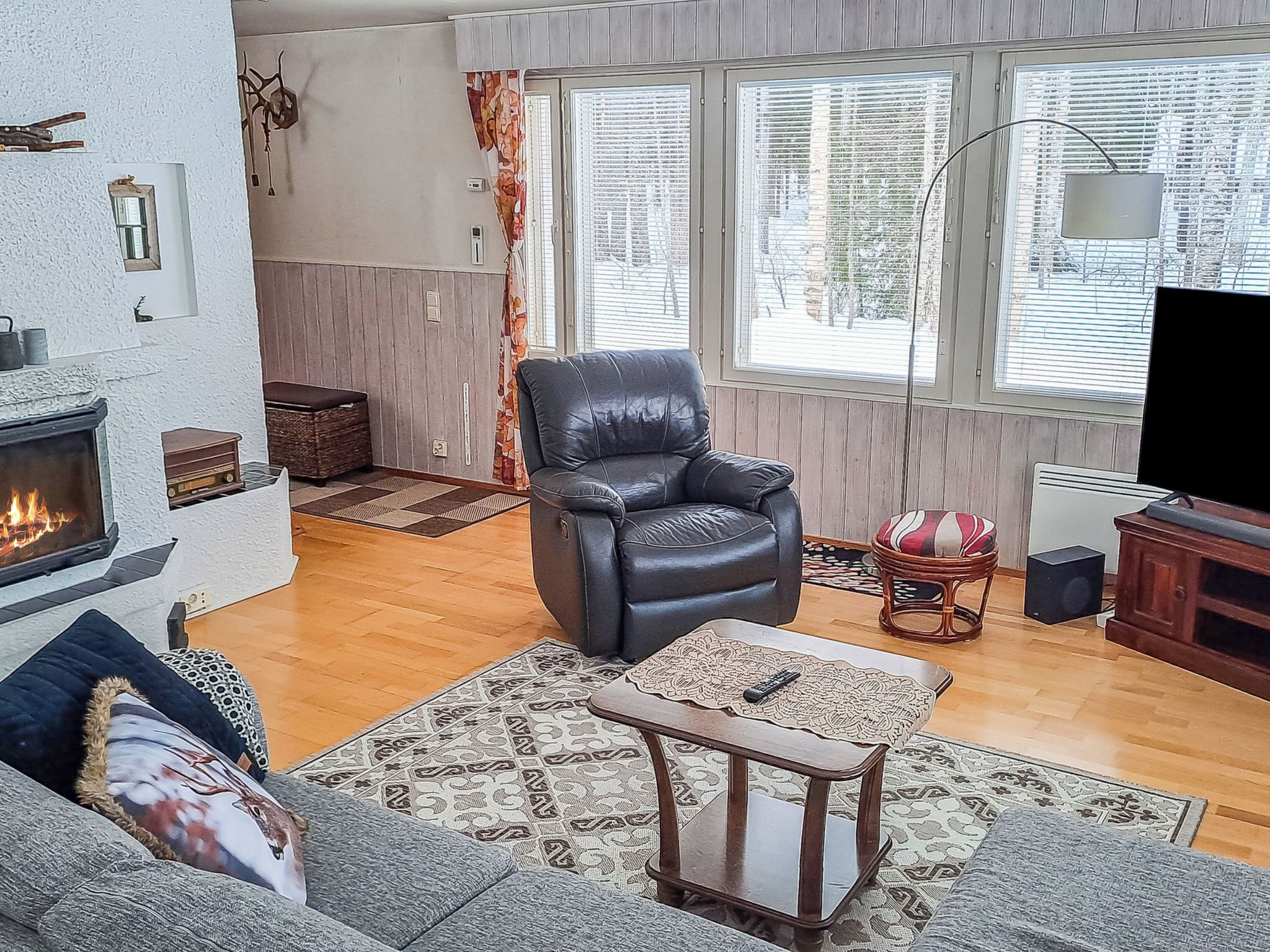 A living room with a fireplace, leather armchair, sofa, patterned rugs, and a television.