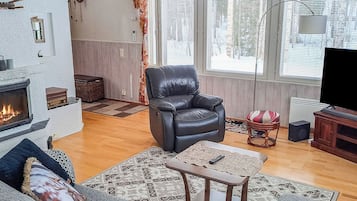 A living room with a fireplace, leather armchair, sofa, patterned rugs, and a television.