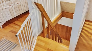 A staircase with wooden steps and white railings, leading to a lower level with a crib. - Koivulahden reinola by Interhome (Ylitornio)