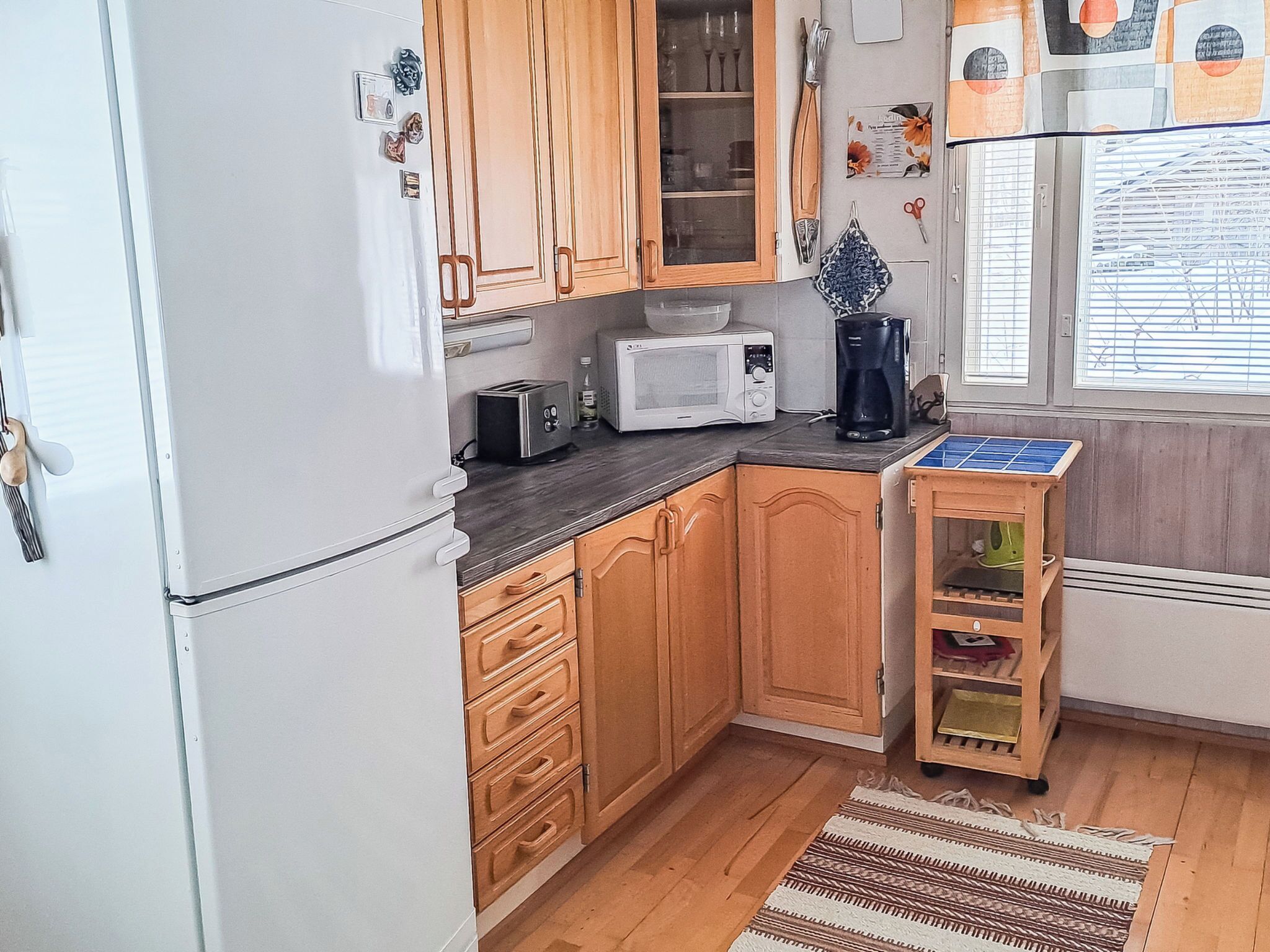 A compact kitchen with wooden cabinets, a microwave, a toaster, and a small wooden table with a solar panel.