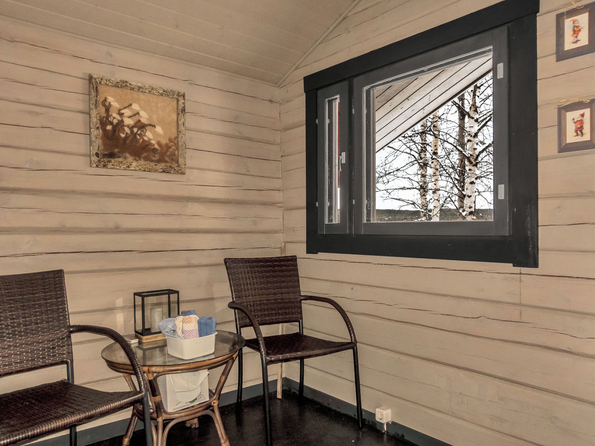 A corner room with a window, two wicker chairs, a small table, and a framed picture on the wall.